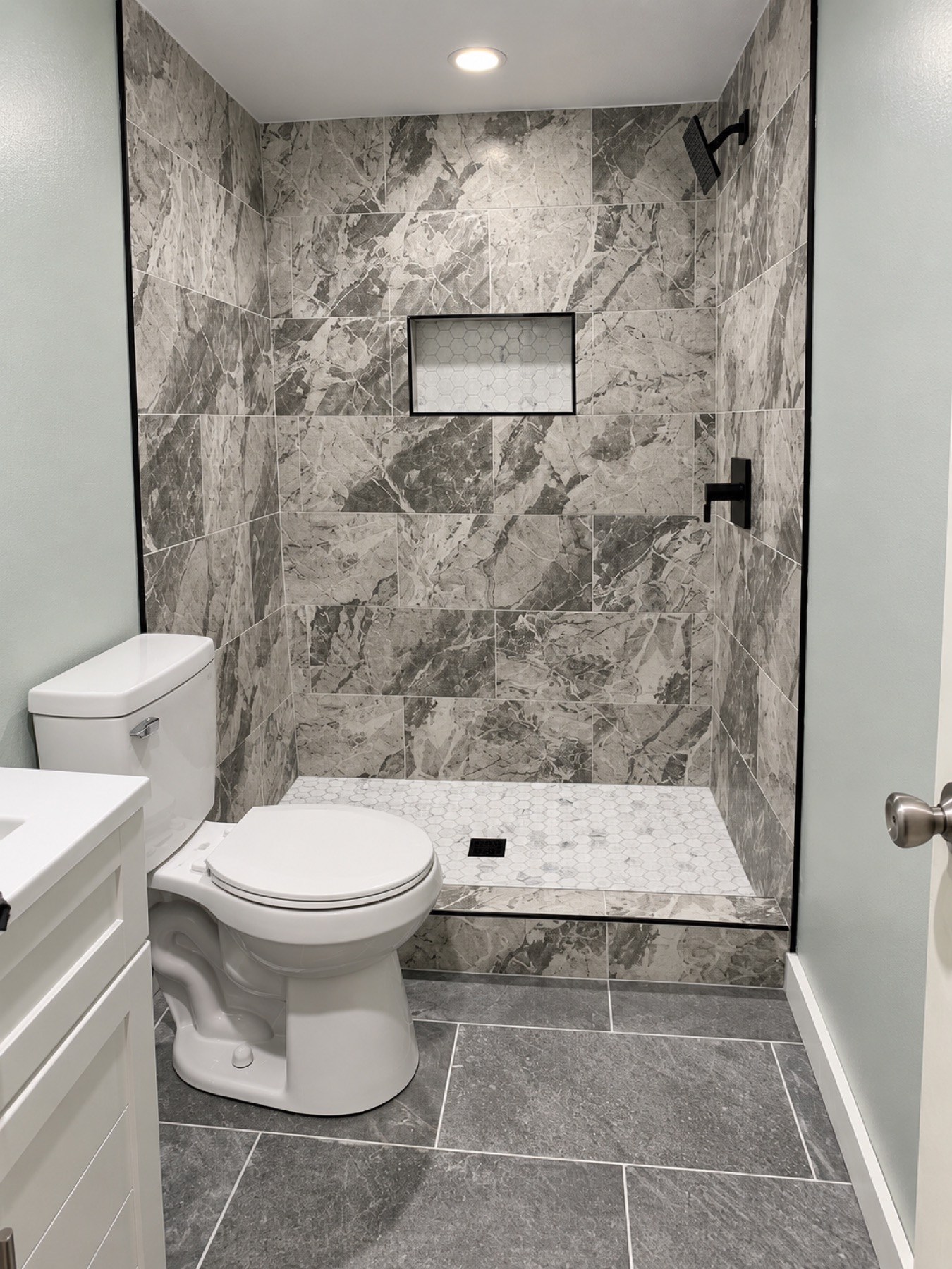 Gray marble look tile shower with black hardware and hexagon floor