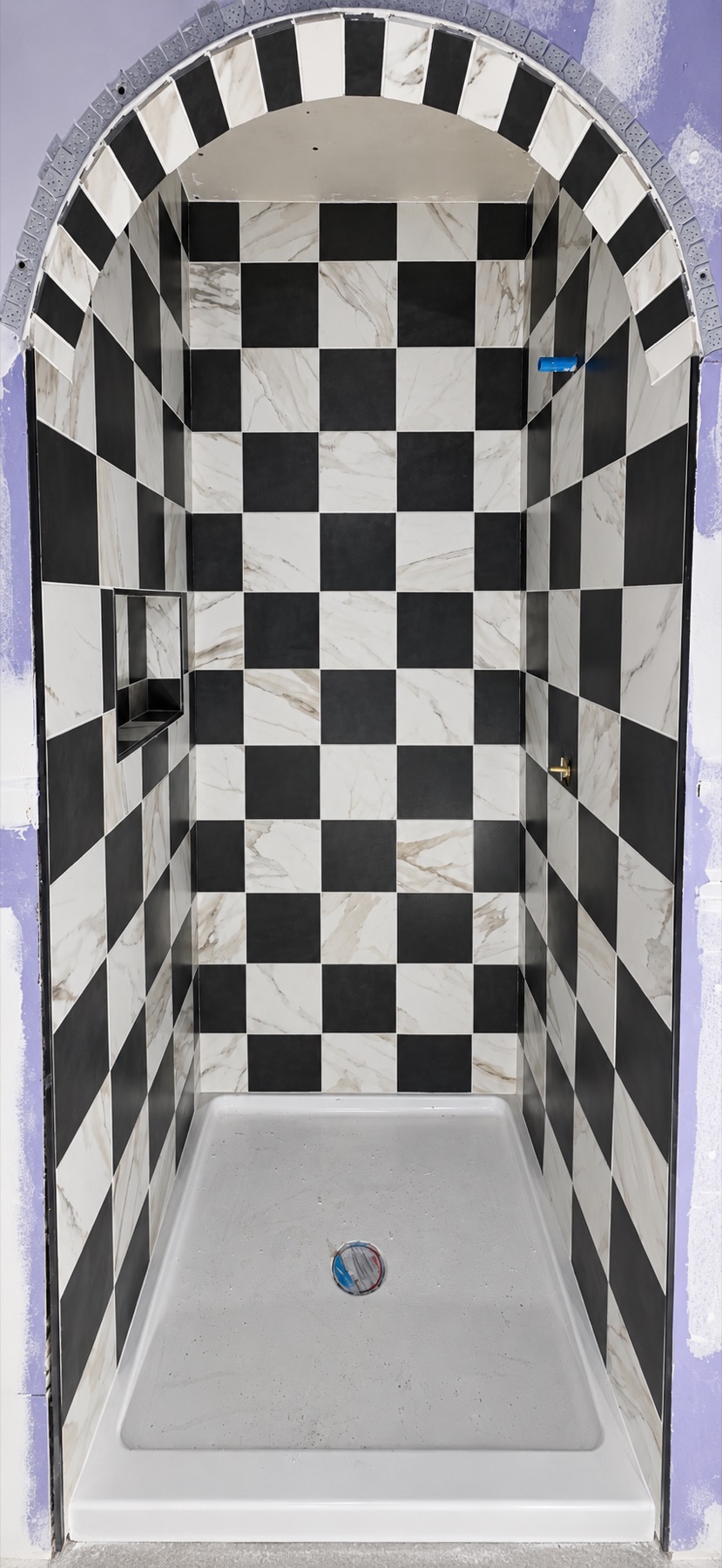 Black and white checkerboard marble tile shower with an arched entry, installed by Ramirez Pro Tile
